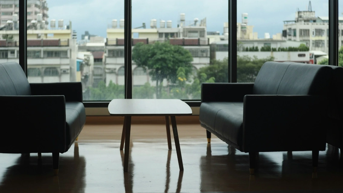 Two black leather sofas facing a small wooden table before a large window